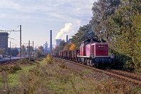 km 2,9  In Blickrichtung Süden kommt nun allmählich der Hochofen sowie Schornsteine und Kühltürme des HKM-Komplexes ins Bild. Auf den folgenden Bildern nähern wir uns dieser Kulisse allmählich. Parallel zur Eisenbahn führt hier die Straßenbahnlinie 904 (heute: 903) nach Hüttenheim, die zum Aufnahemzeitpunkt noch die alten Ausleger besaß. Hier zieht die 290 301 im alten roten Lack einen langen Übergabezug und erreicht gleich den Bahnhof Wanheim (18. Oktober 1989). : Str 2315 DU-Hochfeld Süd - HKM, a - Aufnahmeort, a Deutschland, ao Duisburg, ao Duisburg-Wanheim, eb DB 290 301-1, es 2315 km 2-9