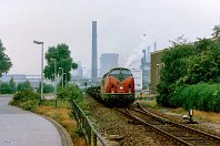 km 3,6  Wiederum 22 Jahre früher und 200 Meter weiter südlich entstand diese Aufnahme am 15. Juli 1986: Die Loklegende 221 129 zieht einen schweren Stahlzug am Anschluss Duisburg Thyssen (EDUT) vorbei. Der markante Schornstein in Bildmitte wurde erst 2007 gesprengt (siehe vorangegangenes Bild). Links ist hier ein verwaister Werksparkplatz zu sehen, auf dem sich heute eine Autowerkstatt befindet. Der Anschluss existiert seit wenigen Jahren wieder für die Bedienung des Containerumschlagplatzes  "Logport II". : 2, 221 (DB V 200.1), Str 2315 DU-Hochfeld Süd - HKM, a - Aufnahmeort, a Deutschland, ao Duisburg, ao Duisburg-Wanheim, eb DB 221 129-0, es 2315 km 3-6