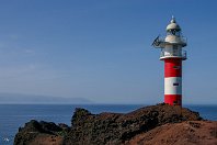 Punta de Teno - Teneriffa (Spanien)  Im Jahre 1976 entstanden drei große neue Leuchttürme auf der Insel Teneriffa, darunter der Faro de Punta de Teno an der äußersten Westspitze auf einer kleinen Vulkaninsel, die sich direkt an die eindrucksvolle Steilküste von Los Gigantes anschließt. Der weiße Betonturm mit zwei roten Streifen ersetzte den deutlich niedrigeren Vorgänger aus dem Jahre 1893, der in unmittelbarer Nachbarschaft auch heute noch steht.  Im Hintergrund grüßt die Nachbarinsel La Gomera herüber (16. Januar 2007). : LT Punta de Teno, Leuchttürme, Seezeichen, a - Aufnahmeort, a Spanien